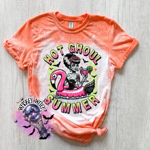A Orange and bleach splattered effect  t-shirt with a graphic of a zombie woman in a flamingo pool float, holding a cocktail. The text "Hot Ghoul Summer" is printed on the shirt.