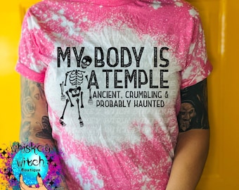 May include: Pink and white tie-dye t-shirt with the text "MY BODY IS A TEMPLE" and a skeleton graphic. The text continues with "ANCIENT, CRUMBLING & PROBABLY HAUNTED". The shirt has rolled-up sleeves.