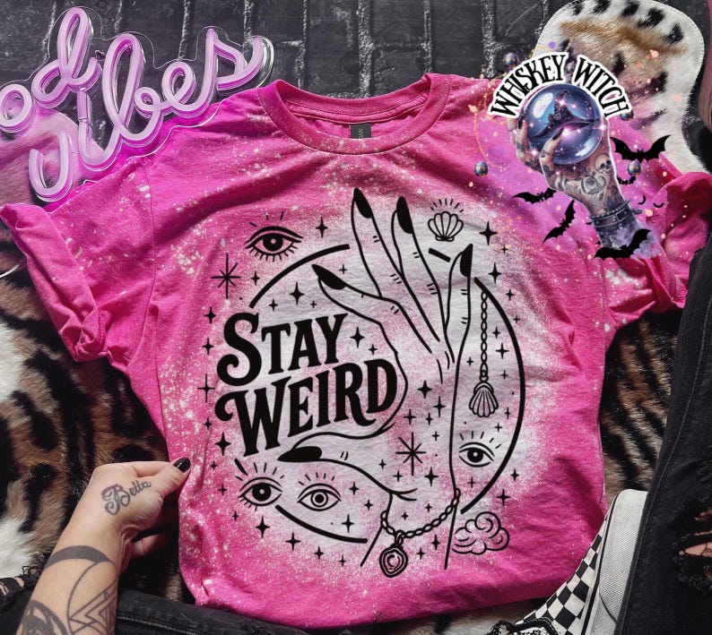 Handmade bleached styles shirt. Close-up of witchy Stay Weird shirt design with celestial artwork, mystical hands, stars, and bold black text