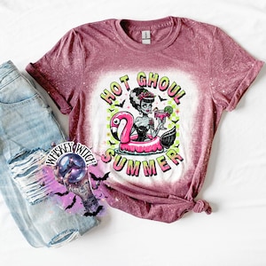 A maroon and bleach splattered effect  t-shirt with a graphic of a zombie woman in a flamingo pool float, holding a cocktail. The text "Hot Ghoul Summer" is printed on the shirt.