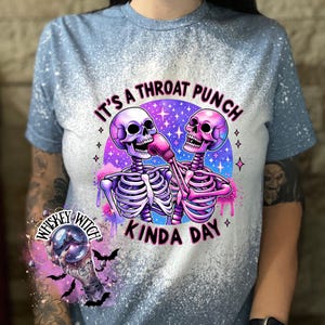 May include: A blue bleached t-shirt with a graphic of two skeletons wearing boxing gloves and the text "It's a throat punch kinda day".