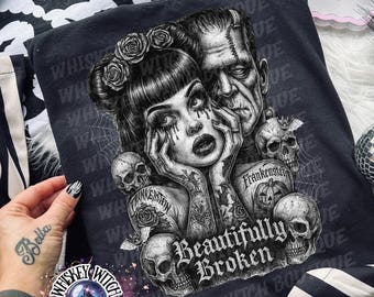 May include: Dark grey t-shirt with a gothic illustration of a woman and Frankenstein's monster, surrounded by skulls and roses. The text "Beautifully Broken" is displayed. The shirt is part of the "Whiskey Witch Boutique" collection.