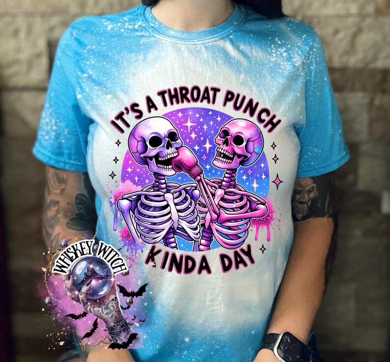 May include: A blue tie-dye t-shirt with a white bleach design featuring two skeletons boxing with the text "It's a throat punch kinda day".