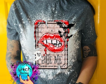 May include: A grey t-shirt with a bleach-splattered design featuring a red vampire mouth with fangs and the text "Bite Me". A ghost and bats are also visible in the design. The shirt is from Whiskey Witch Boutique.