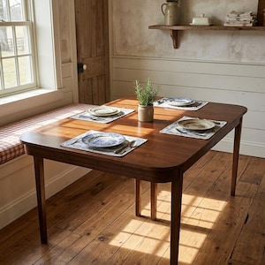 May include: A wooden dining table with four place settings, each with a blue and white patterned plate, a placemat, and silverware. A small potted plant sits in the center. The table is set on a hardwood floor.