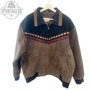 May include: A brown and black suede jacket featuring a front zipper closure, a pointed collar, and a decorative band across the chest with a yellow diamond pattern and a maroon Greek key design. The jacket has black ribbed cuffs and hem.