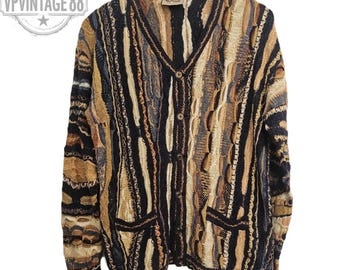 Könnte beinhalten: Ein Vintage-Strickcardigan mit Knopfleiste und einem einzigartigen strukturierten Design. Der Pullover hat einen V-Ausschnitt, zwei Vordertaschen und eine Mischung aus braunen, beigen, schwarzen und blauen vertikalen Streifen. Der Pullover hängt vor einem weißen Hintergrund.