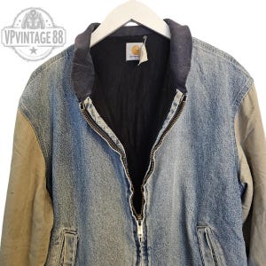 Pu&ograve; includere: Giacca di jeans vintage con chiusura a zip completa. La giacca presenta un corpo in denim blu, maniche beige e fodera nera. Il colletto &egrave; in maglia a coste grigio scuro. Il logo Carhartt &egrave; visibile. Capo classico.