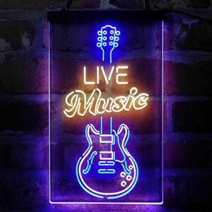 May include: A neon sign featuring a blue and white guitar outline and the words "LIVE Music" in a stylized font. The sign is rectangular with a black border, set against a brick wall.