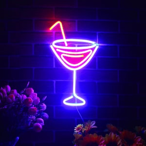 May include: A neon sign shaped like a cocktail glass with a straw. The glass is outlined in bright blue, with a pink interior and a yellow straw. The sign is mounted on a dark brick wall, with flowers in the foreground.