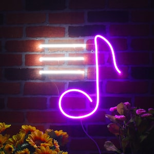 Può includere: Un'insegna al neon a forma di nota musicale e tre linee orizzontali, che si illumina di viola e bianco. L'insegna è montata su un muro di mattoni rossi, con fiori gialli e viola in primo piano.