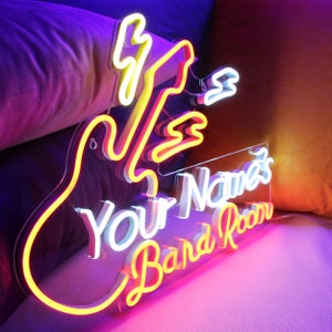 Puede incluir: Letrero de neón con forma de guitarra con el texto "Your Name's Band Room" en neón blanco y amarillo.