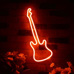 Peut inclure: Une enseigne de guitare au néon orange est fixée sur un mur de briques rouges. Le contour de la guitare brille vivement, créant une ambiance chaleureuse. L'image comprend des fleurs en bas, ajoutant une touche décorative. Pour les amateurs de musique.