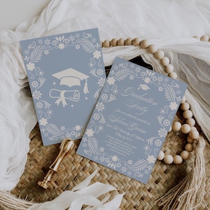 May include: Two blue graduation party invitations with floral borders and a mortarboard and diploma illustration. One invitation reads "Graduation Party" and includes event details. A gold wax seal and wooden beads are also present.