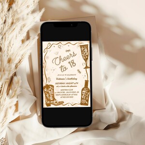 Puede incluir: Un tel&eacute;fono inteligente muestra una invitaci&oacute;n de color beige con el texto "Cheers to 18". La invitaci&oacute;n presenta una bota de vaquero, una copa de champ&aacute;n y una ilustraci&oacute;n de botella. La invitaci&oacute;n es para el cumplea&ntilde;os de Victoria, el s&aacute;bado 19 de agosto.