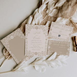 May include: A collection of beige wedding stationery with floral border designs. The invitation features the names "Frida and Carlos" and event details. Additional cards include "Save The Date" and a response card. A gold wax seal is visible.