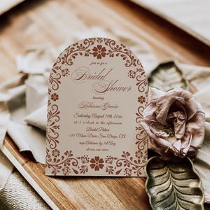May include: A bridal shower invitation with floral accents and the text "Bridal Shower" and event details. The invitation is on a wooden tray with a dried rose and a decorative leaf.