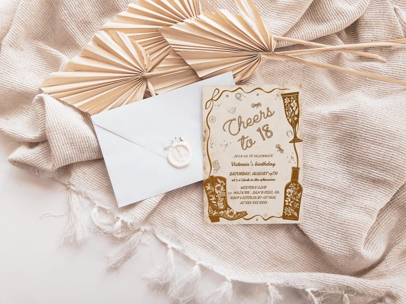 Puede incluir: Una tarjeta de invitaci&oacute;n con el texto "Cheers to 18" y detalles del evento, con una ilustraci&oacute;n de bota de vaquero y copa de vino. Un sobre blanco con un sello de cera est&aacute; junto a la tarjeta, con hojas de palma beige secas sobre una tela beige.