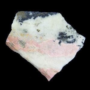 Puede incluir: Primer plano de una roca blanca, rosa y negra con textura rugosa. La roca tiene un aspecto estratificado con vetas rosas y negras.