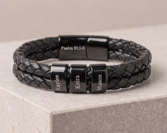 May include: A black braided leather bracelet featuring three rectangular black metal beads engraved with the names Kaylee, Keira, and Mason, and a black metal clasp engraved with the text Psalm 91:1-6, creating a layered, textured appearance.