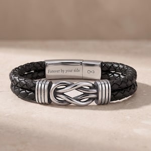 Può includere: Un bracciale in pelle intrecciata nera con una chiusura in metallo color argento incisa con il testo Forever by your side e un simbolo dell'infinito. Il centro del bracciale presenta un nodo decorativo in metallo color argento con scanalature.