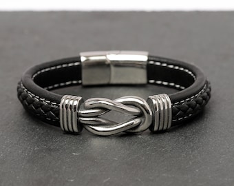 May include: A black leather bracelet with a silver knot clasp. The bracelet has a braided leather design and a magnetic closure.