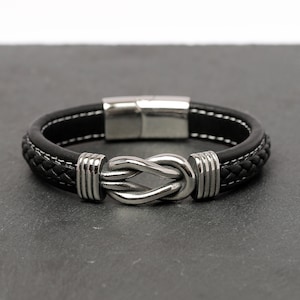 May include: A black leather bracelet with a silver knot clasp. The bracelet has a braided leather design and a magnetic closure.