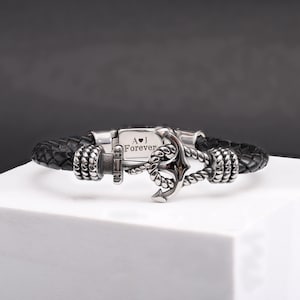 以下が含まれることがあります： シルバーのアンカーチャームと「A♥J Forever」というパーソナライズされた刻印が施された、黒い革のブレスレットです。