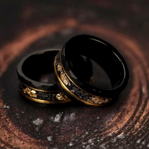 May include: Two black tungsten carbide rings with gold inlay. The rings are stacked on top of each other.