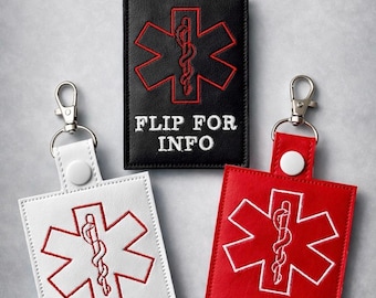 May include: Three rectangular medical alert keychains in black, white, and red. Each features an embroidered Star of Life symbol and text. The black and red tags read "FLIP FOR INFO," while the white tag reads "INFO ON BACK."