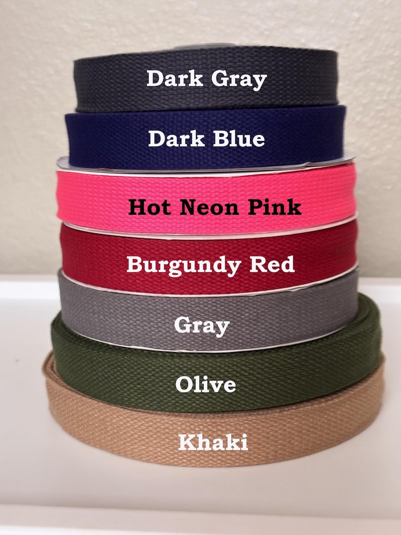 May include: A stack of seven rolls of woven cotton webbing tape in various colors, labeled with text: Dark Gray, Dark Blue, Hot Neon Pink, Burgundy Red, Gray, Olive, and Khaki. Each roll features a distinct twill texture and solid color.