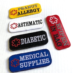 May include: Embroidered medical alert patches in yellow, white, black, red, and blue. Text includes "PEANUT ALLERGY", "ASTHMATIC", "DIABETIC", "EPIPEN IN BAG", and "MEDICAL SUPPLIES". Each patch features a red medical symbol.