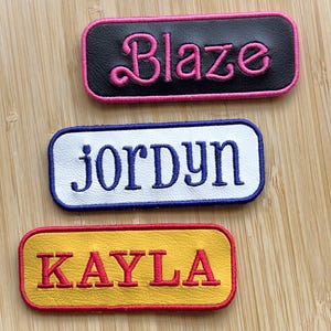 May include: Three embroidered name patches. The top patch is black with pink text that reads "Blaze". The middle patch is white with blue text that reads "Jordyn". The bottom patch is yellow with red text that reads "Kayla".