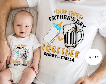 May include: White t-shirts with a graphic design of a baby bottle and a beer mug with the text "Our First Father's Day Together Daddy and Stella".