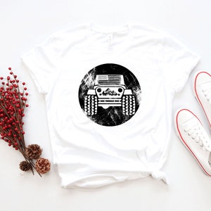 May include: White t-shirt with a black and white graphic of a Jeep with an American flag on the front. The Jeep is surrounded by a distressed circle.