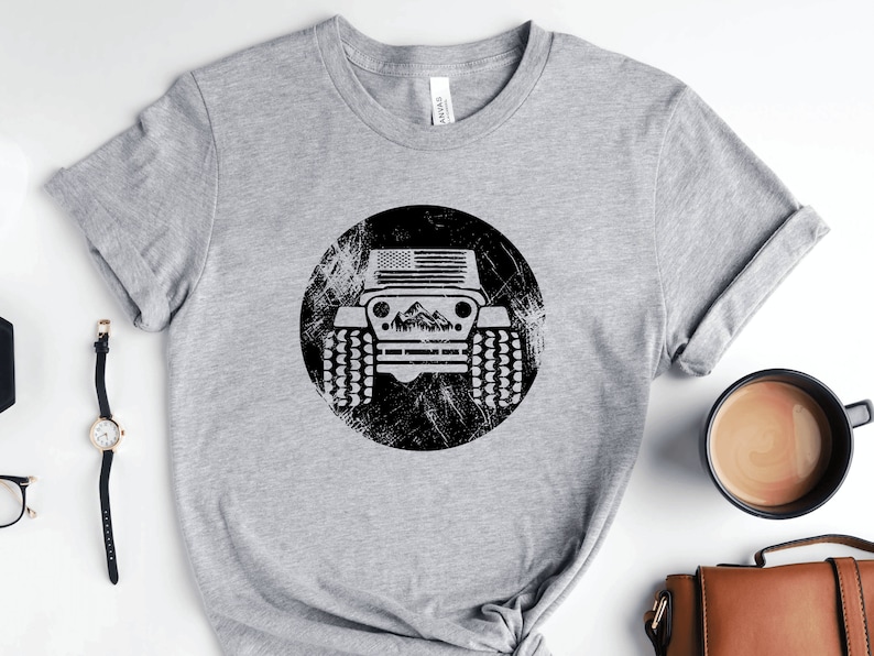 May include: Gray t-shirt with a black and white graphic of a jeep with an American flag on the hood. The jeep is in a circle with a distressed background.