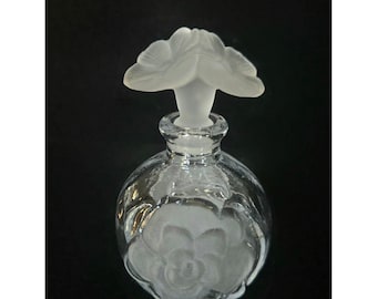 Frasco de perfume Glass Act Studio com tampa fosca em formato de flor e detalhes florais.