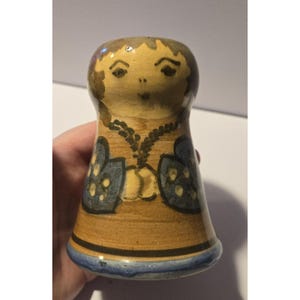 Könnte beinhalten: Handbemalte Keramikfigur in Form einer Person. Die Figur hat einen beigefarbenen Körper, einen hellbraunen Kopf und blaue Akzente. Das Gesicht hat bemalte Merkmale. Die Figur ist etwa 10 cm hoch.
