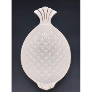 May include: White ceramic pineapple-shaped serving dish with gold trim. The dish has a textured diamond pattern on the body and a detailed top. The serving dish is designed for decorative or functional use.