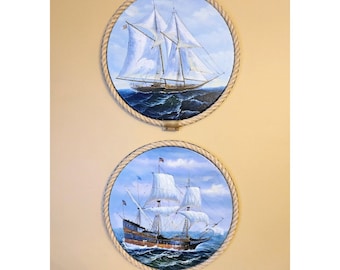Puede incluir: Dos pinturas redondas enmarcadas de barcos de vela en una pared beige. La pintura superior presenta un barco de vela blanco con un cielo azul y blanco y agua azul. La pintura inferior presenta un barco de vela marrón con un cielo azul y blanco y agua azul.