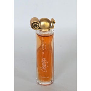 May include: A tall, cylindrical glass perfume bottle filled with amber liquid. The bottle features the text Givenchy Paris Organza Parfum printed on the front. It is topped with a decorative, metallic gold cap shaped like a stylized scroll.