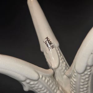 May include: Close-up of a white ceramic object with a textured surface. The object has multiple pointed projections. The words "MADE IN JAPAN" are printed in black on one of the projections.