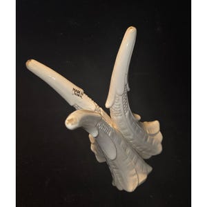May include: Off-white ceramic antler-shaped decorative piece. The piece has a textured surface and is marked "MADE IN JAPAN". The antlers are arranged in a V-shape, with detailed carvings and a smooth, glossy finish. The piece is likely a decorative item.