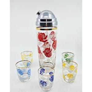 May include: A vintage cocktail shaker set featuring a tall glass shaker with a silver lid and gold trim, and six matching shot glasses. The set is decorated with red, blue, yellow, and green rose patterns.