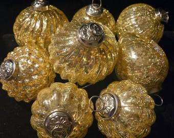 May include: A collection of eight gold-colored Christmas ornaments. Each ornament has a textured, ribbed surface and a silver-colored metal cap with a loop for hanging. The ornaments are spherical and vary slightly in shape.