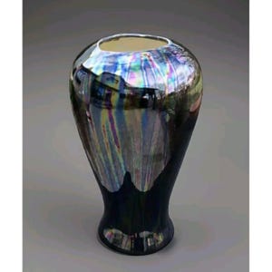 Puede incluir: Un jarrón de cerámica negro con un esmalte iridiscente. El esmalte tiene un efecto arcoíris con tonos de azul, morado y verde.