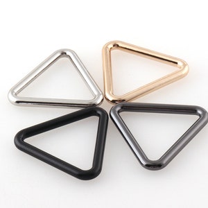 May include: Four triangle-shaped metal rings in silver, gold, black, and gunmetal.