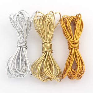 Puede incluir: Tres madejas de cordón elástico metálico en plata, oro y bronce. Cada madeja está bien envuelta en el centro, con los extremos del cordón abriéndose en abanico. Los cordones tienen una calidad brillante y reflectante, adecuados para manualidades y joyería.