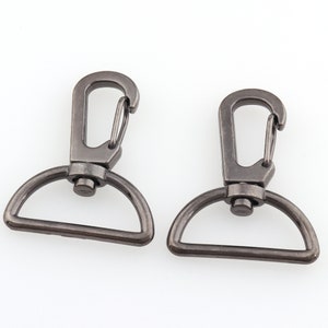 Könnte beinhalten: Zwei silberfarbene Metall-Schwenkverschlüsse mit einem D-Ring. Die Verschlüsse sind offen und bereit, an einem Band oder einer Kette befestigt zu werden.