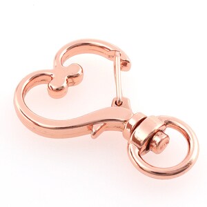 May include: Rose gold heart-shaped swivel clasp with a round ring. This metal clasp is perfect for attaching to keychains, bags, or other accessories.